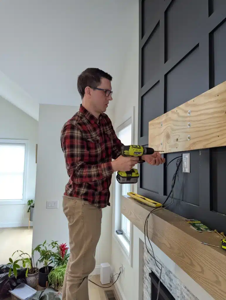 Horus Community Services technician drilling a wood backer board onto a black accent wall above a fireplace in Trumansburg, NY