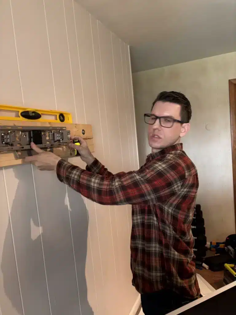 Horus Community Services technician using a level to set a wood backer board for a TV wall mount in Trumansburg, NY
