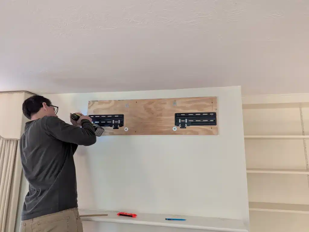 Horus Community Services technician fastening wood backer boards high on a wall for a TV mount in Trumansburg, NY