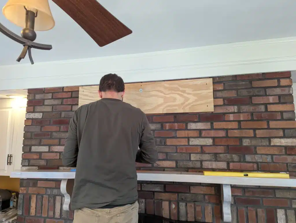Horus Community Services technician attaching a plywood backer board to a brick fireplace in Trumansburg, NY
