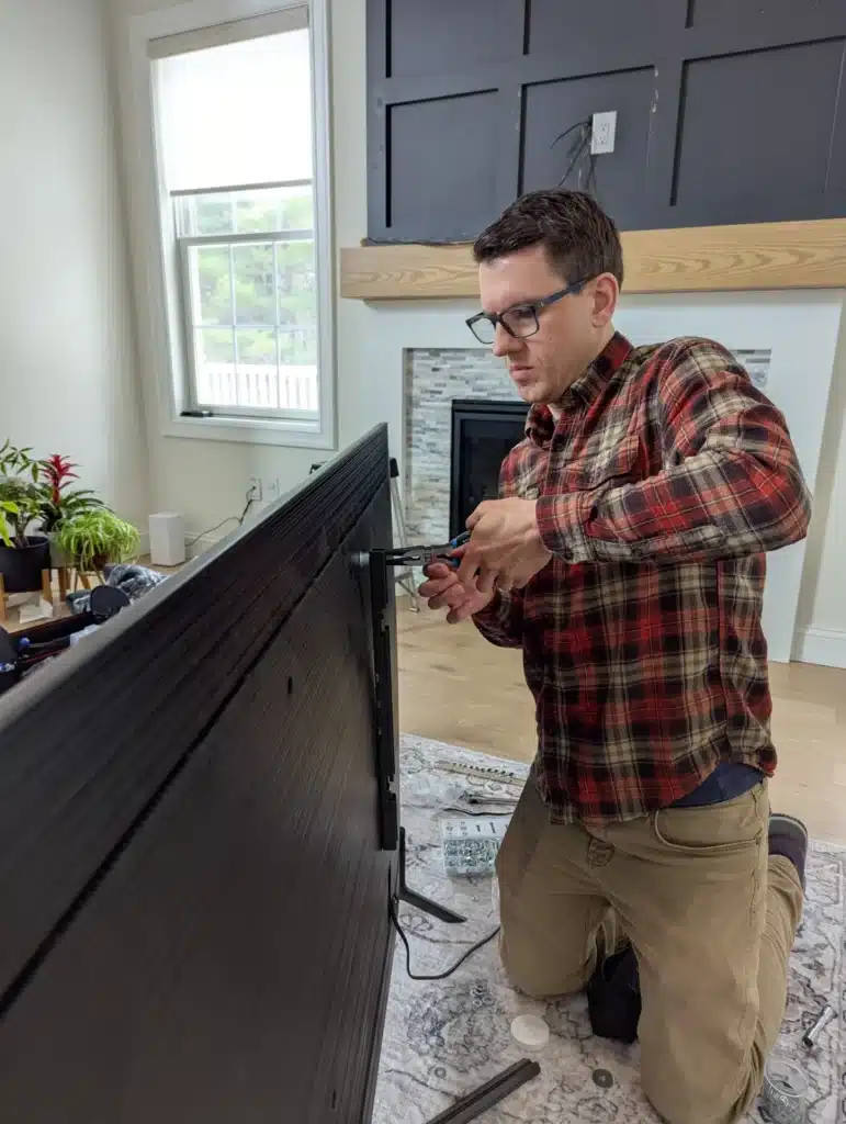 Horus Community Services technician connecting cables behind a TV mounted above a fireplace in Trumansburg, NY