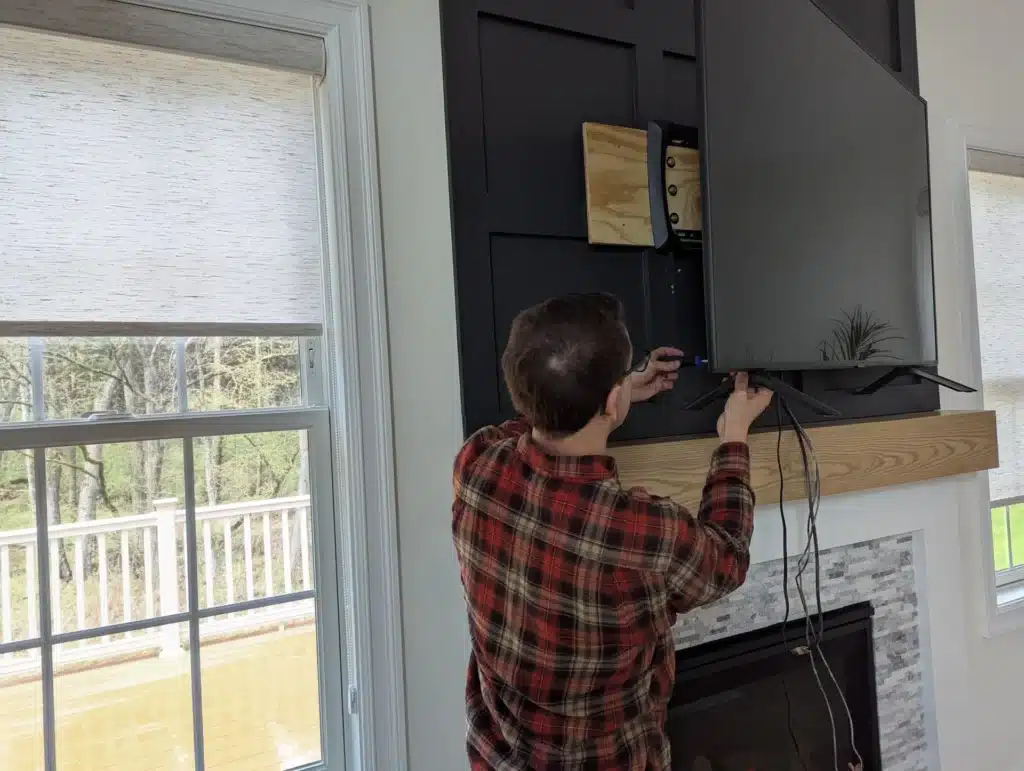 Horus Community Services technician routing cables behind a TV on a fireplace accent wall in Trumansburg, NY