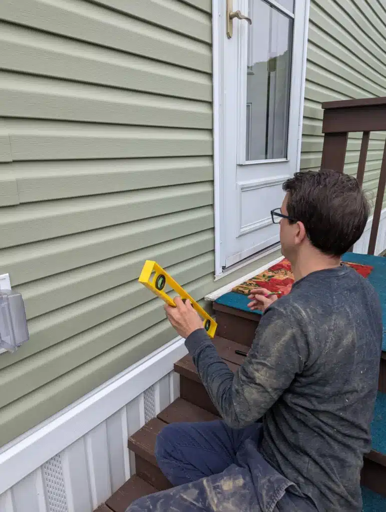 Horus Community Services technician leveling against exterior siding for a cable entry in Trumansburg, NY
