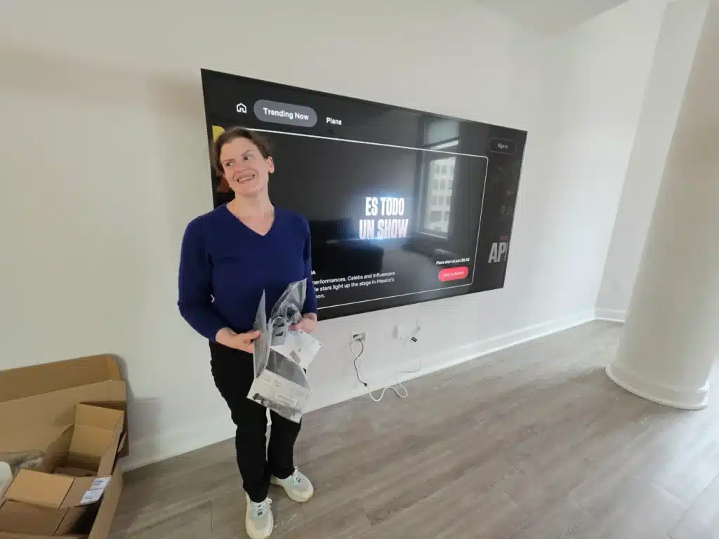 Smiling homeowner next to a newly wall-mounted TV installed by Horus Community Services in Trumansburg, NY