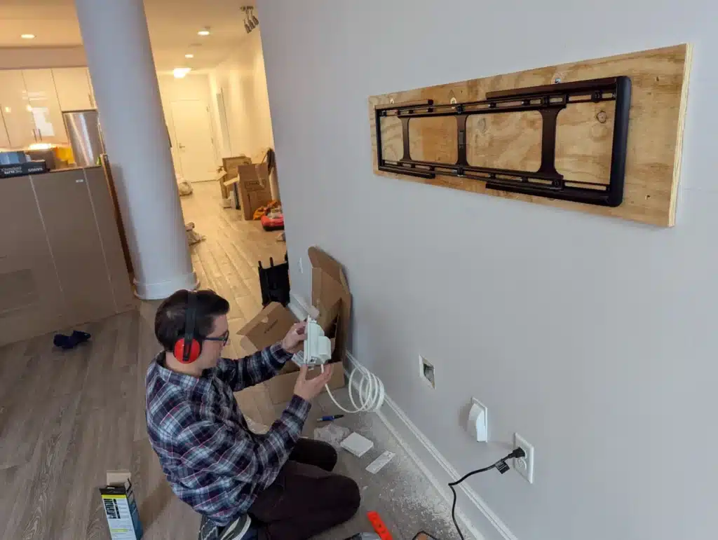 Horus Community Services technician running in-wall cables below a TV mount bracket in a Trumansburg, NY condo