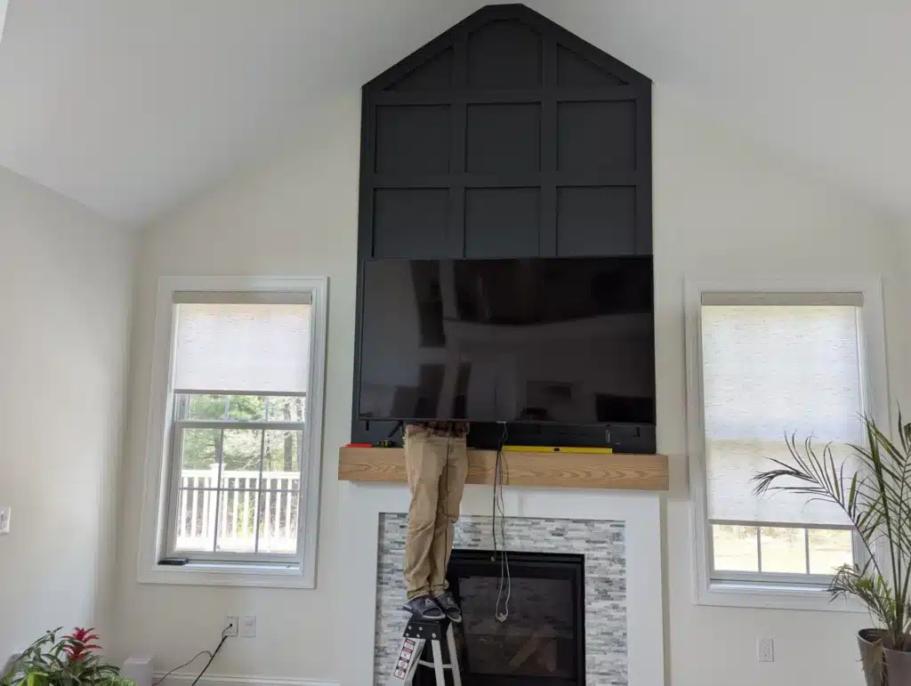 Horus Community Services installing a large TV on a tall board-and-batten accent wall above a stone fireplace in a vaulted Trumansburg, NY living room