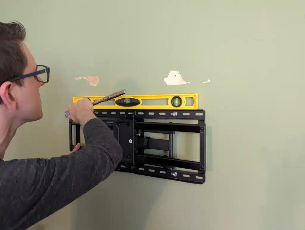 Horus Community Services technician leveling a full-motion TV mount bracket on a wall in Trumansburg, NY
