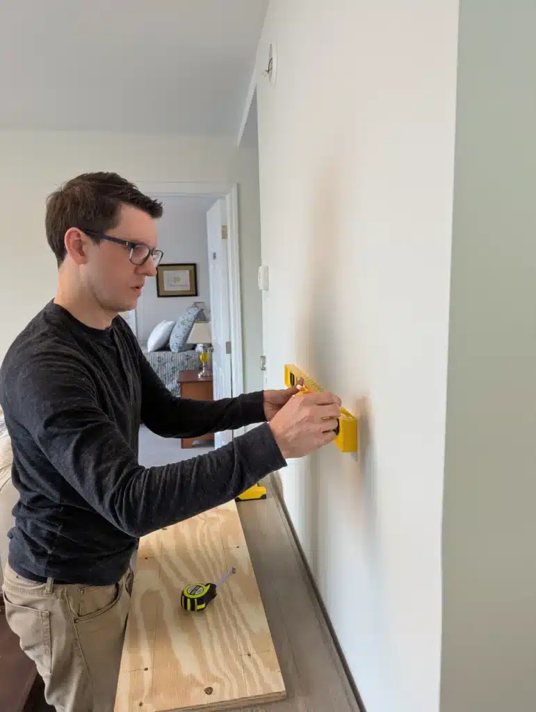 Horus Community Services technician marking mounting points on a hallway wall in Trumansburg, NY