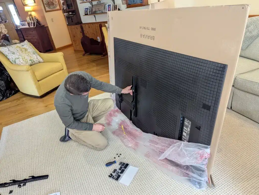 Horus Community Services technician attaching a wall-mount bracket to the back of a large TV in Trumansburg, NY