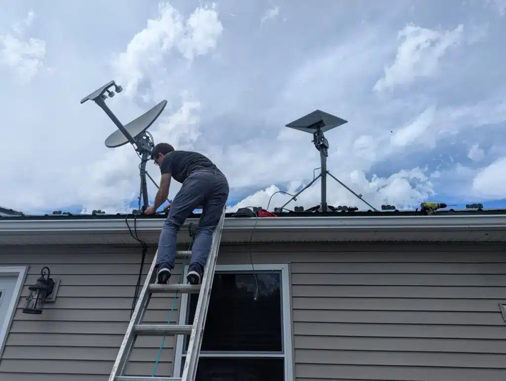 Horus Community Services technician installing a Starlink dish beside existing satellite dishes on a roof in Trumansburg, NY
