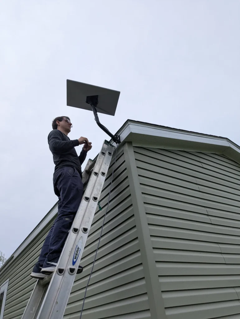 Horus Community Services technician mounting a Starlink satellite dish at a roof gable in Trumansburg, NY
