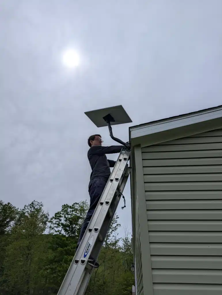 Horus Community Services technician installing a Starlink dish sidewall mount from a ladder in Trumansburg, NY