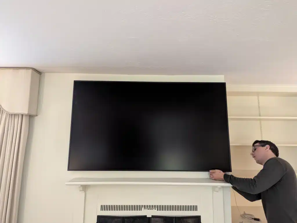 Horus Community Services technician mounting a large TV above a white fireplace mantel in Trumansburg, NY