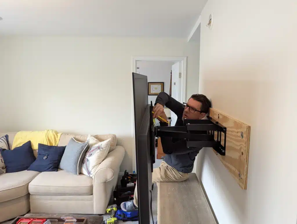Horus Community Services technician mounting a TV bracket on a living room wall in Trumansburg, NY