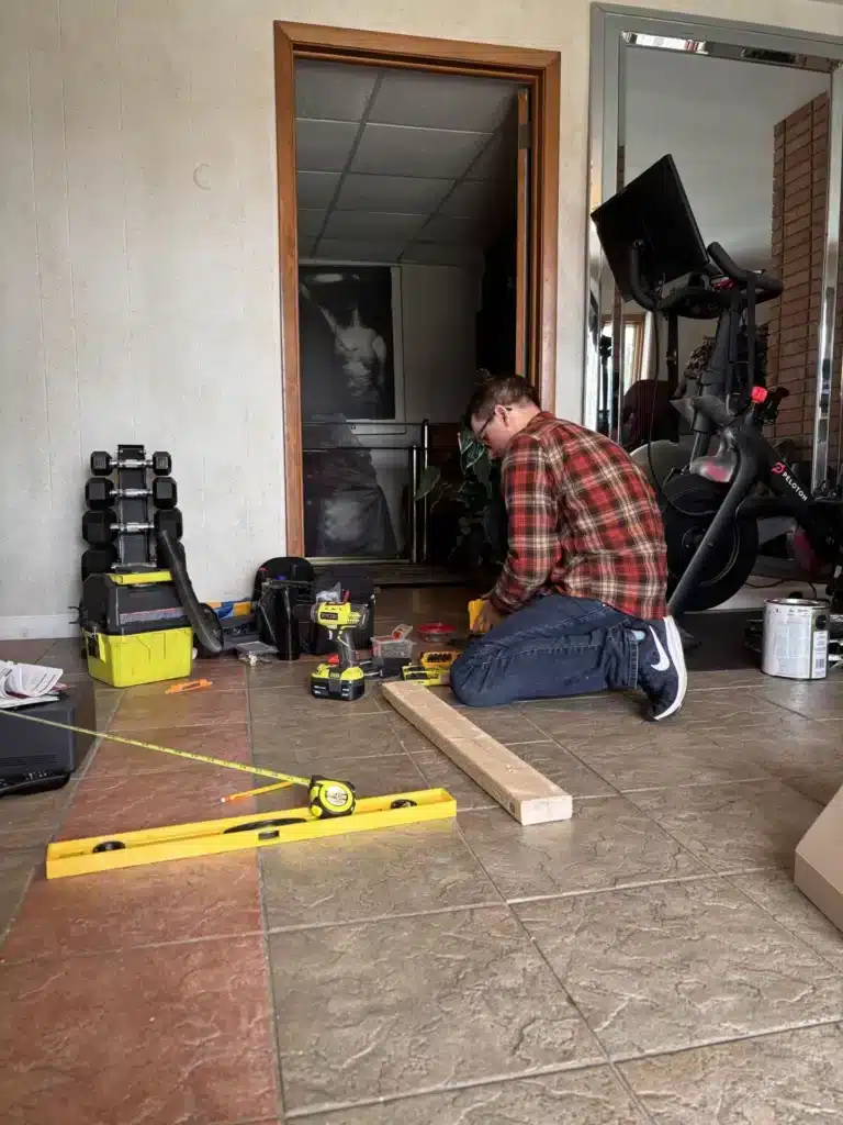 Horus Community Services technician with drills, levels and gear preparing to mount a large TV near an entryway in Trumansburg, NY