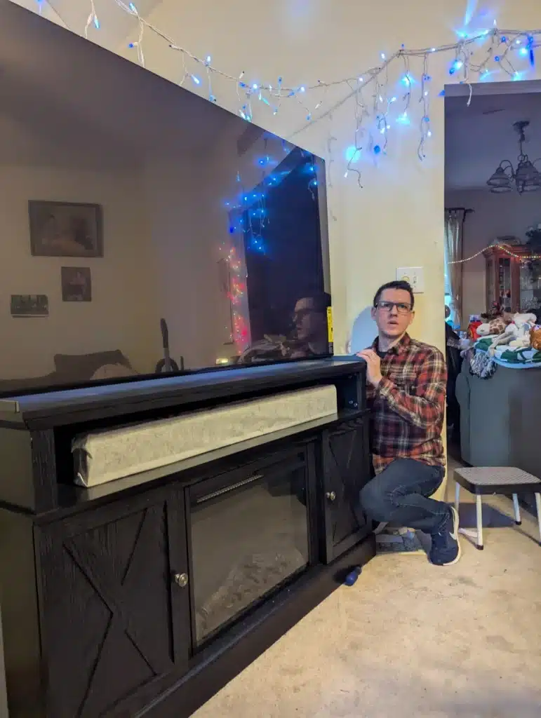 Horus Community Services technician beside a large TV wall-mounted above an electric fireplace media console in a Trumansburg, NY living room