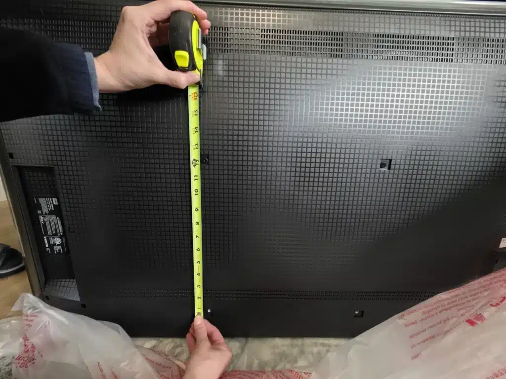 Horus Community Services technician measuring the back of a TV for wall-mount bracket placement in Trumansburg, NY