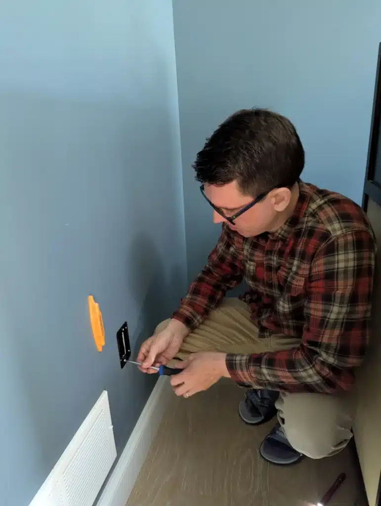 Horus Community Services technician marking a wall near the baseboard for a TV mount and cable routing in Trumansburg, NY