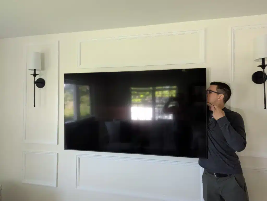Horus Community Services technician checking a wall-mounted TV on a framed living room wall in Trumansburg, NY
